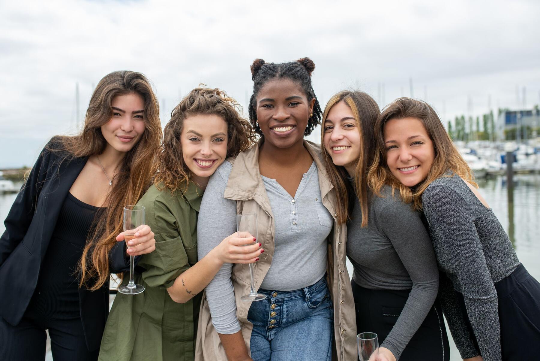 Five smiling women friends posing together by the marina